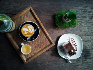 Top view of a cup of coffee with cup of tea and chocolate cake on wooden plate.