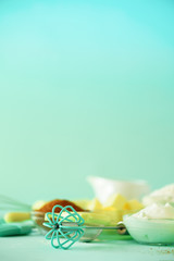 Bakery food frame, cooking concept. Different baking ingredients - butter, sugar, flour, milk, eggs, oil, spoon, rolling pin, brush, whisk over blue background. Copy space