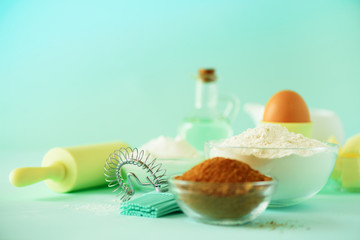 Fototapeta na wymiar Healthy baking ingredients - butter, sugar, flour, eggs, oil, spoon, rolling pin, brush, whisk, milk over blue background. Bakery food frame, cooking concept. Copy space.