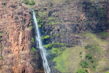 Tall waterfall cascading down a rocky cliff in tropical landscape scene in Kauai Hawaii