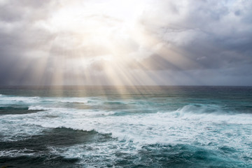Rays of sunlight break through storm clouds above the open ocean waves in a heavenly seascape © deberarr