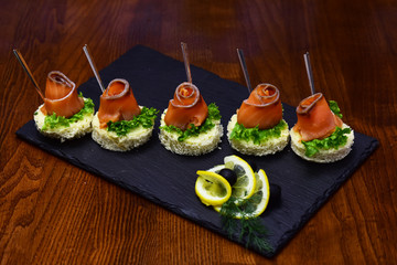 Serving sanape with salmon on slate. Tasty small bread loafs and salmon fish fillet rolls. We speak the good food language