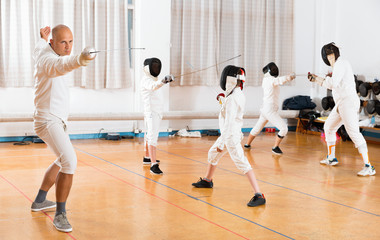 Coaches demonstrating to young athletes attack movements with rapier during fencing workout