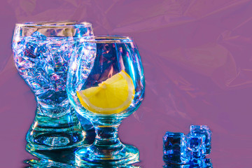 Two glasses with a slice of lemon and ice in blue tones on a lilac background