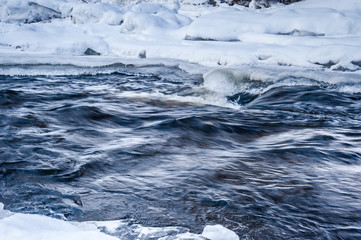 Spring thawed patch in the ice of the river. Frozen ice and snow by the river side. Natural background. Long exposure.