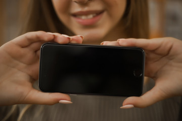 Smiling young student schoolgirl lady with long hair standing in empty classroom showing display of mobile phone. Focus on smartphone.
