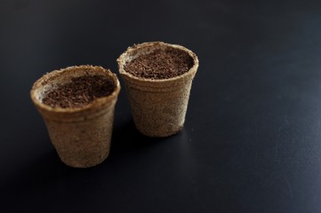 Pots with soil for planting seedlings on black background with copy space