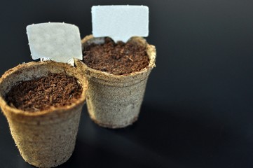 Pots with soil for planting seedlings with indicator plates on black background with copy space