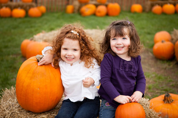 Happy Little Girls Sitting in Pumpkin Patch