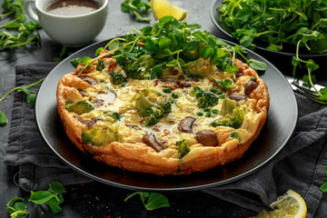 Homemade Frittata with mushrooms, broccoli, feta cheese, green peas and bacon on black plate