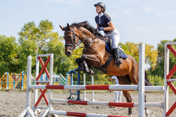 Young horse rider girl jumping over a hurdle on show jumping competition