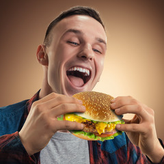 Young handsome man eating a hamburger. Portrait of a happy guy with a hamburger in his hands. Advertising fast food. Tasty cheeseburger.