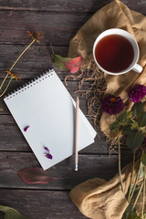 Autumn flatlay on wooden backdrop with a cup of tea and fallen dry yellow, red leaves, flowers. Free space for text.