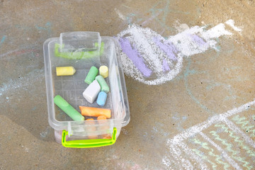 Crayons of blue, green, yellow, white in plastic box. Painted with colored crayons floor tiles in park. Childrens drawing on sidewalk. Childrens leisure concept.