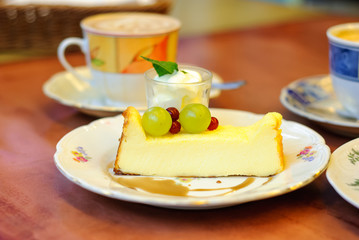 A beautiful, cheesecake with berries, and cream decorated with mint leaves served in magnificent crockery on a wooden table.