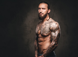Portrait of a shirtless bearded tattooed male. Isolated on dark textured background.