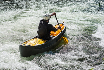 Paddling whitewater open canoe through the rapids .