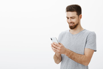 What pleasure looking at bank account full of money. Portrait of delighted stylish and handsome male model with beard holding smarpthone looking at cellphone screen with joy and cheerful smile