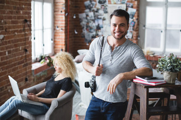 Fototapeta premium Smiling man in a grey t-shirt and jeans standing and a woman sitting with a laptop in loft.