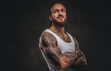 Fototapeta na wymiar Brutal bearded tattooed male in white shirt posing with crossed arms. Isolated on a dark textured background.