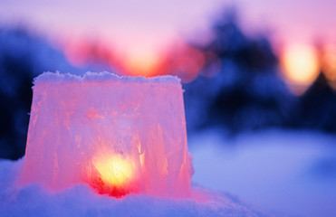 Ice lantern with red candle burning in winter evening twilight.