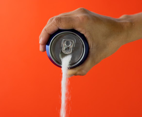 Hand holding a soda can pouring sugar