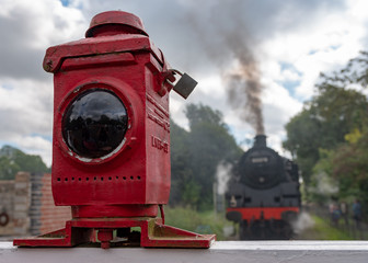 Railway crossing light with steam locomotive in the background