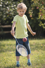 Six years old boy play with racket and ball in the garden