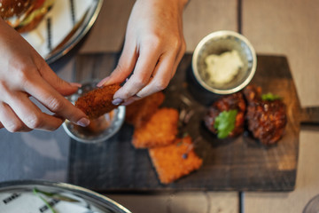 Close up of woman hands holding fried cheese and dipping it into a sauce.