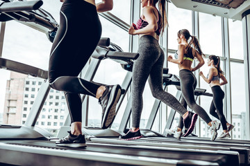Side view of young beautiful women looking away while running on treadmill at gym