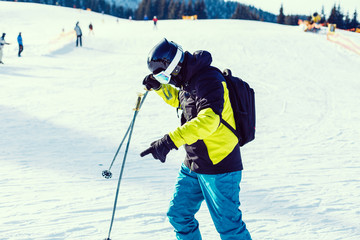 Fototapeta na wymiar Skier holding ski and looking at beautiful snow covered mountains. Young man thinking and looking snowy mountain with copy space. Side view of winter skier guy with mask holding ski equipment outdoor.