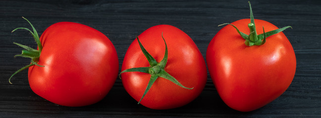 red tomatoes on a green branch on a black wooden background