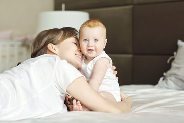 Happy mother hugging baby lying on the bed indoors. Mothers day.