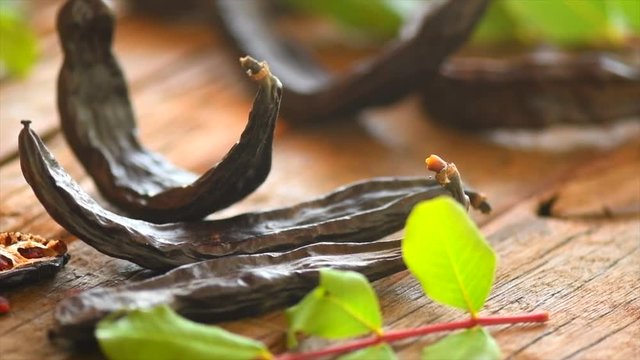 Carob. Healthy organic sweet carob pods with seeds and leaves on a wooden table. Healthy eating, food background. Slow motion. 3840X2160 4K UHD video footage