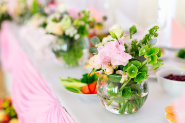A close-up of a round transparent vase with flowers and green tw