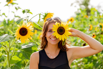Laughing young woman holds a sunflower in front of her eyes