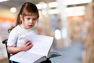 Cute little schoolgirl in glasses on library background