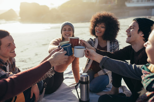 Multi-ethnic friends toasting coffee mugs at the beach
