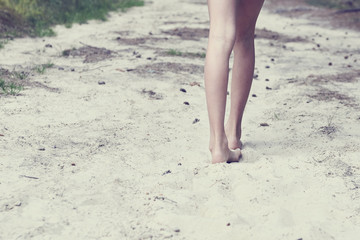 Child girl bare feet walking along the forest sandy path. 