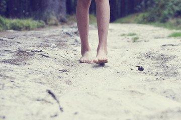 Child girl bare feet walking along the forest sandy path. 