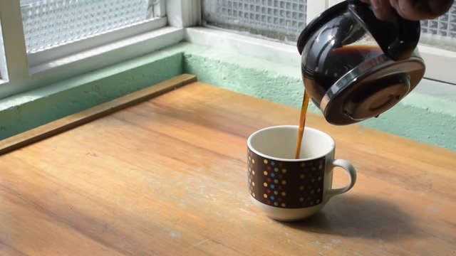 taza con cafe sobre una mesa de madera al lado de una ventana