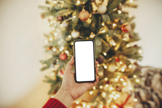 christmas mockup with space for text. christmas advertising, app template. hand holding phone with empty screen on background of golden beautiful christmas tree with lights