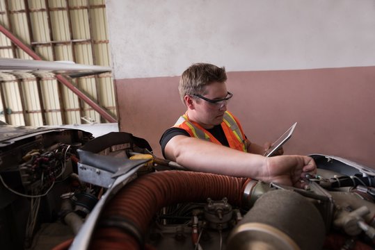 Mechanic using digital tablet while servicing aircraft engine - Powered by Adobe