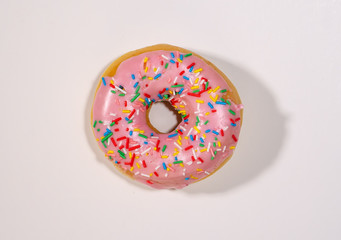 Top view studio photo of a delicious and tempting pink strawberry donut with colorful sprinkles isolated on white background in unhealthy nutrition and sugar addiction concept.