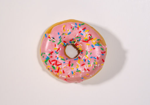 Top view studio photo of a delicious and tempting pink strawberry donut with colorful sprinkles isolated on white background in unhealthy nutrition and sugar addiction concept.