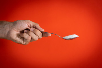 Woman hand holding and offering a spoon full of sugar isolated on a red background in sugar...