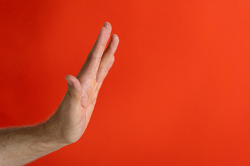 Studio photo of a strong man hand showing stop gesture and sign isolated on a red background in...