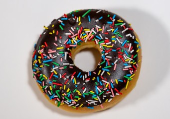 Top view studio photo of a delicious and tempting chocolate donut with colorful sprinkles isolated on white background in unhealthy nutrition and chocolate and sugar addiction concept.