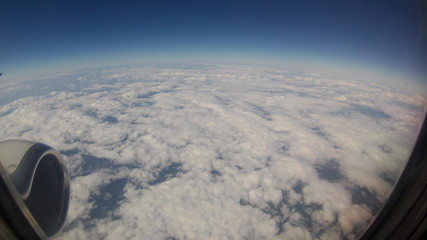 View from passenger's seat in airplane flying above clouds