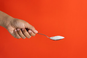 Woman hand holding and offering a spoon full of sugar isolated on a red background in sugar...